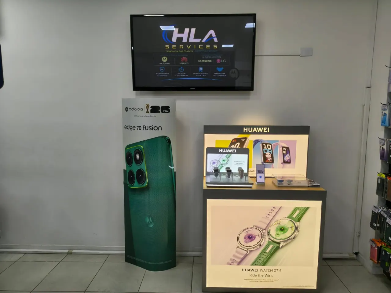 Vitrine da HLA Services com painel das marcas atendidas e displays Motorola e Huawei